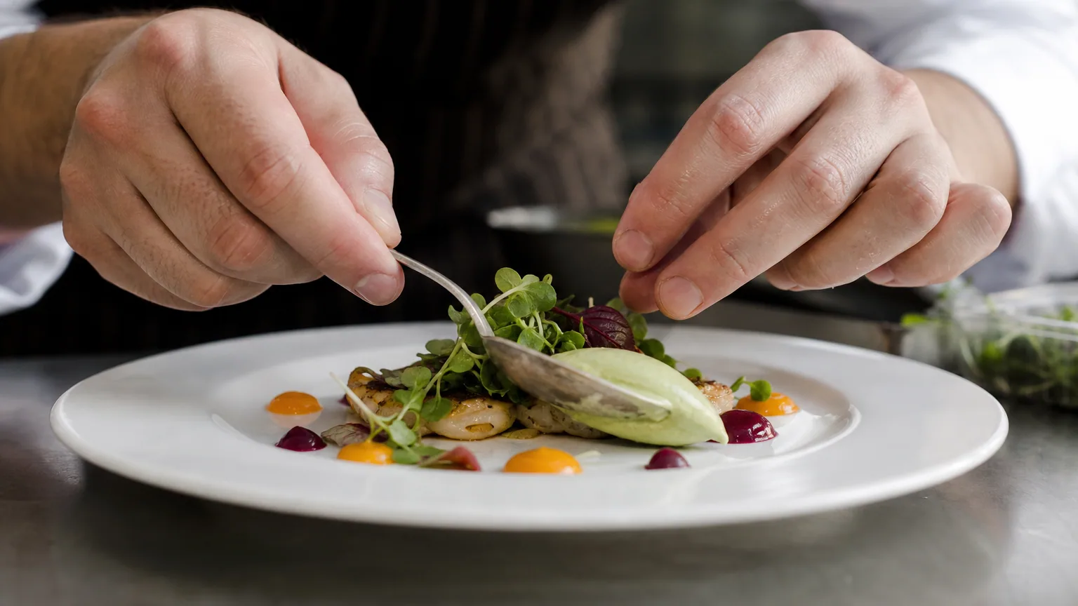 Les mains d'un chef dressant délicatement une assiette gastronomique avec une cuillère