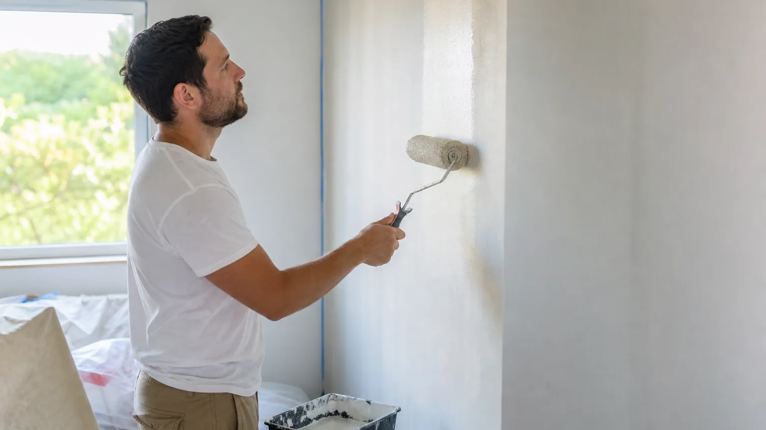 Une personne peint un mur intérieur au rouleau dans une lumière naturelle douce