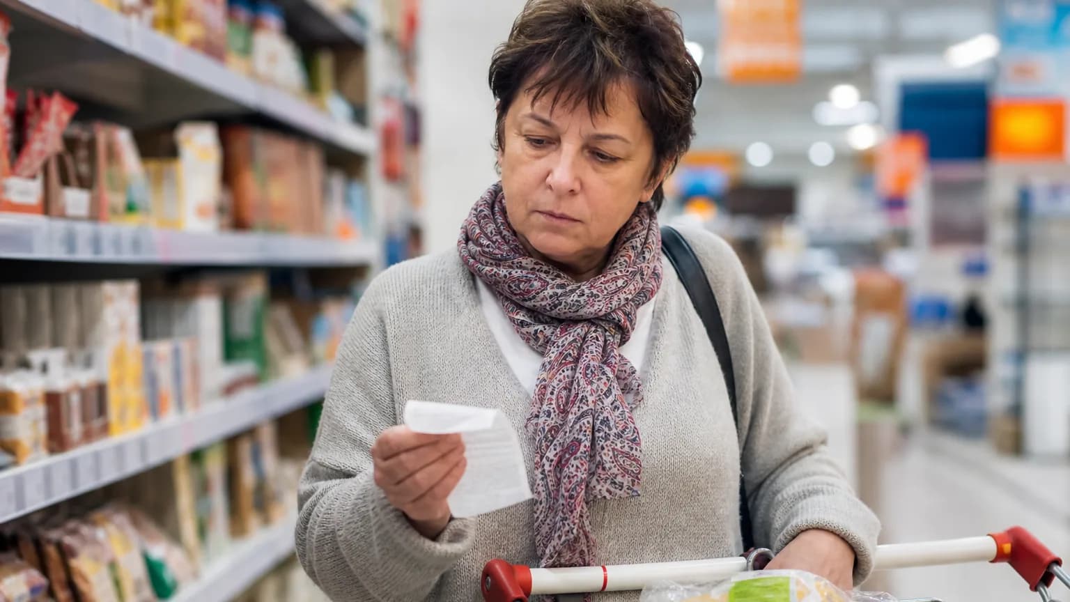 Une femme examine son ticket de caisse dans un supermarché, l'air préoccupé par la hausse des prix.