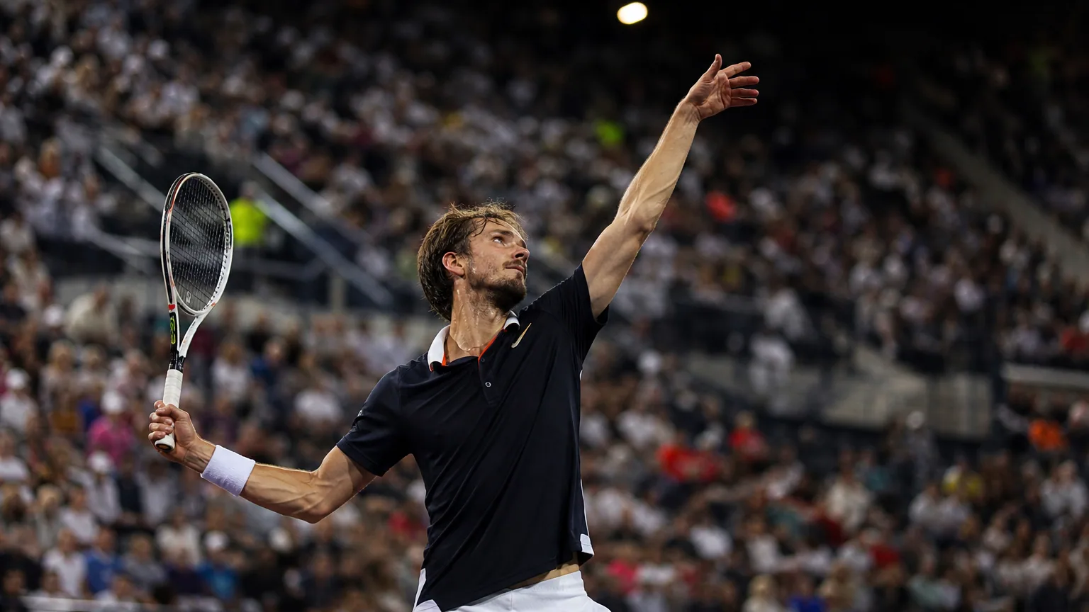 Un joueur de tennis au service dans un grand stade illuminé lors d'un tournoi ATP