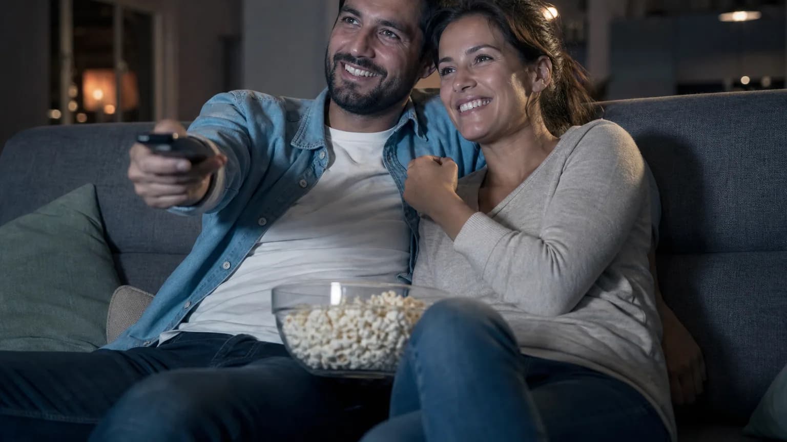 Un couple regarde une série le soir dans son salon, éclairé par la lumière de la télévision