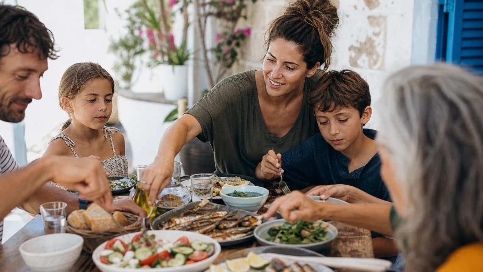 Table conviviale garnie de légumes frais, poisson grillé, olives et huile d'olive partagée en famille